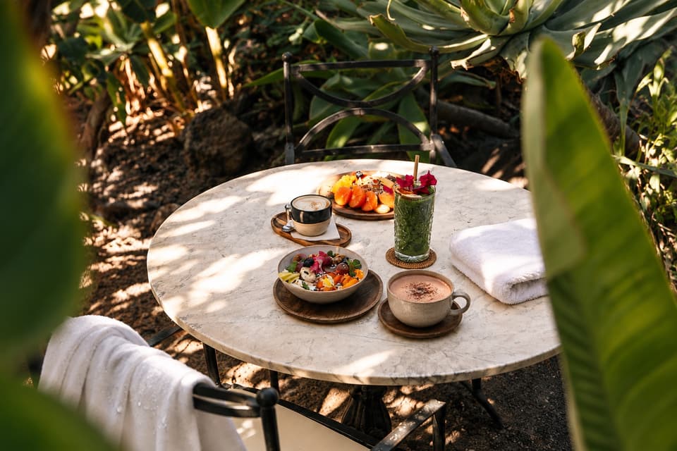 Mesa de mármol entre plantas con fruta, bebidas calientes y toallas