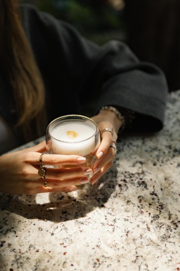 Manos que sostienen un café con espuma sobre una mesa de granito