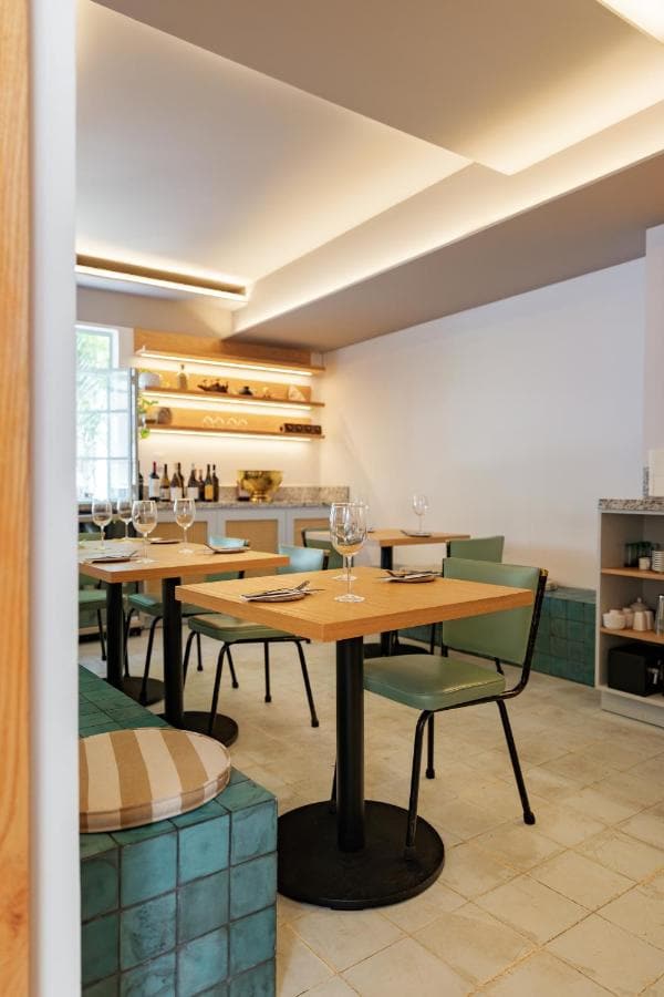 El comedor de Calma: mesas de madera, sillas verdes y repisas iluminadas