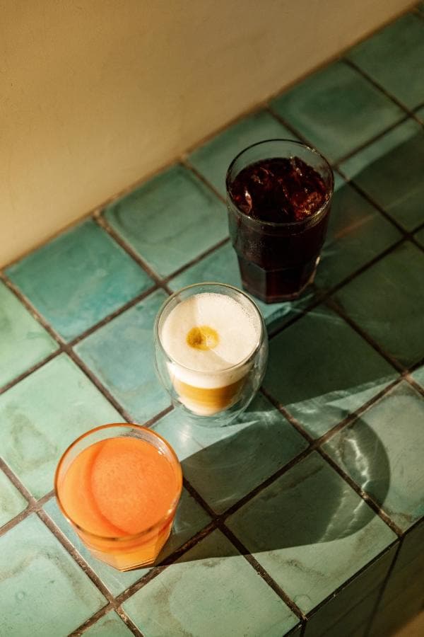 Café, jugo y una bebida roja sobre una barra de azulejo verde