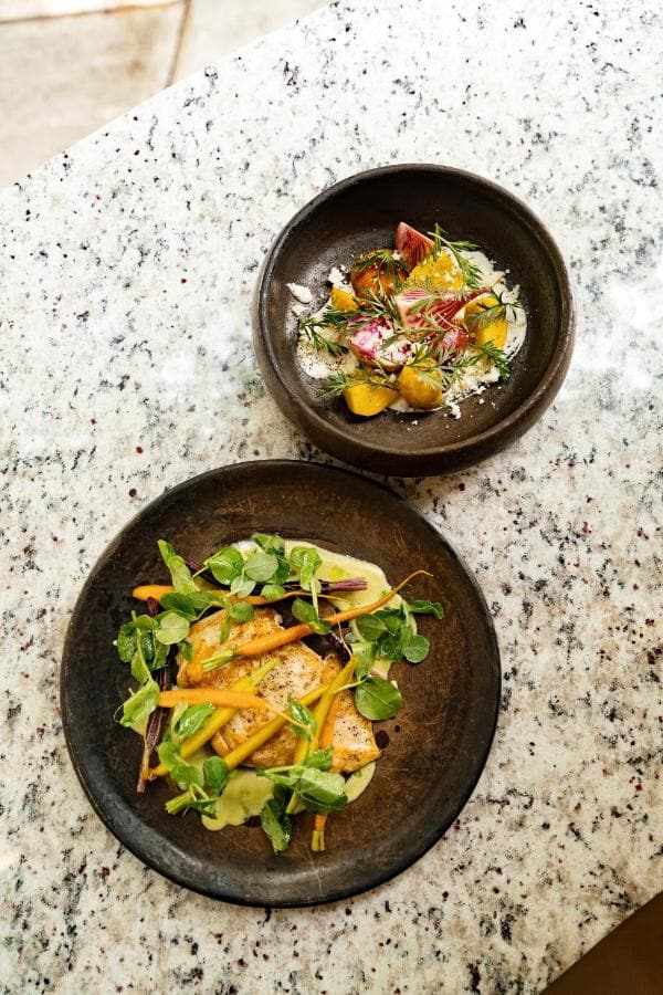 Dos platos de verduras y flores sobre una mesa de granito
