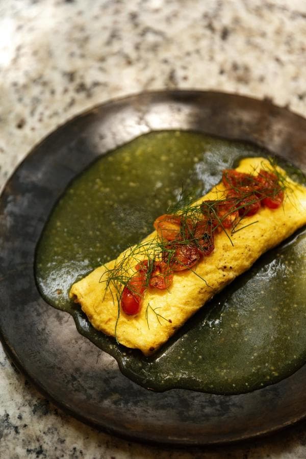 Un omelette con jitomate sobre salsa verde, en plato de barro
