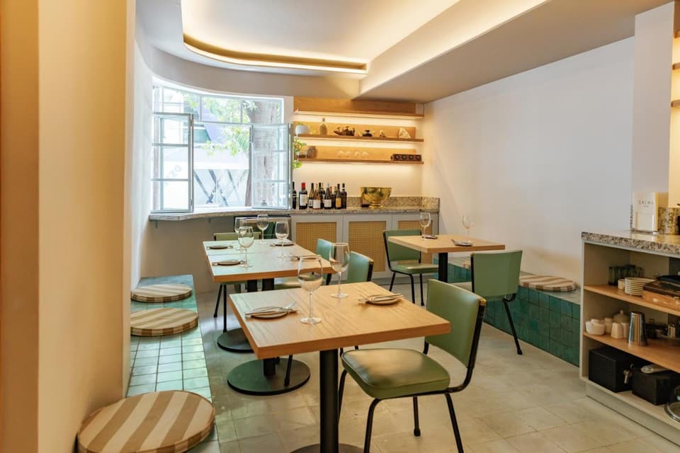 El comedor de Calma: mesas de madera, sillas verdes, repisas iluminadas y un ventanal curvo