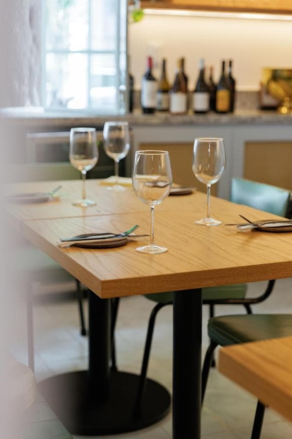 Mesas de madera con copas, y botellas de vino en la repisa de Calma