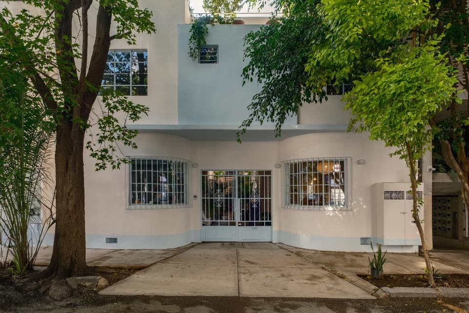 Fachada blanca de los años treinta en Calle Cholula 21, con dos ventanales curvos bajo los árboles