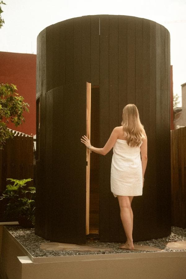 Una huésped en toalla abre la puerta del sauna, una torre de madera negra en la azotea